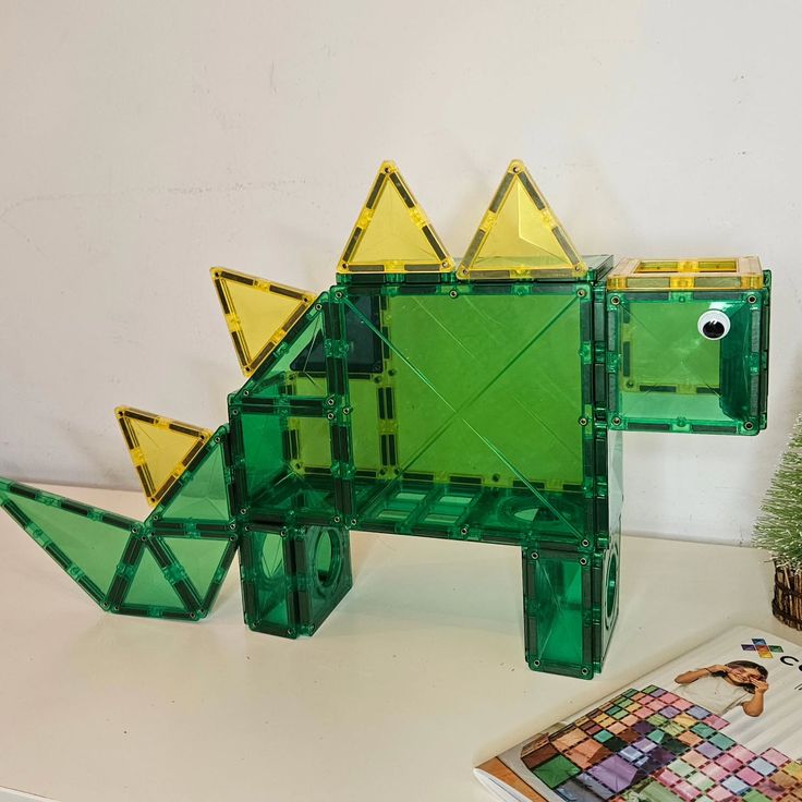 Driedimensionale groene dinosaurus van magnetische tegels met gele stekels en een wiebeloog.
